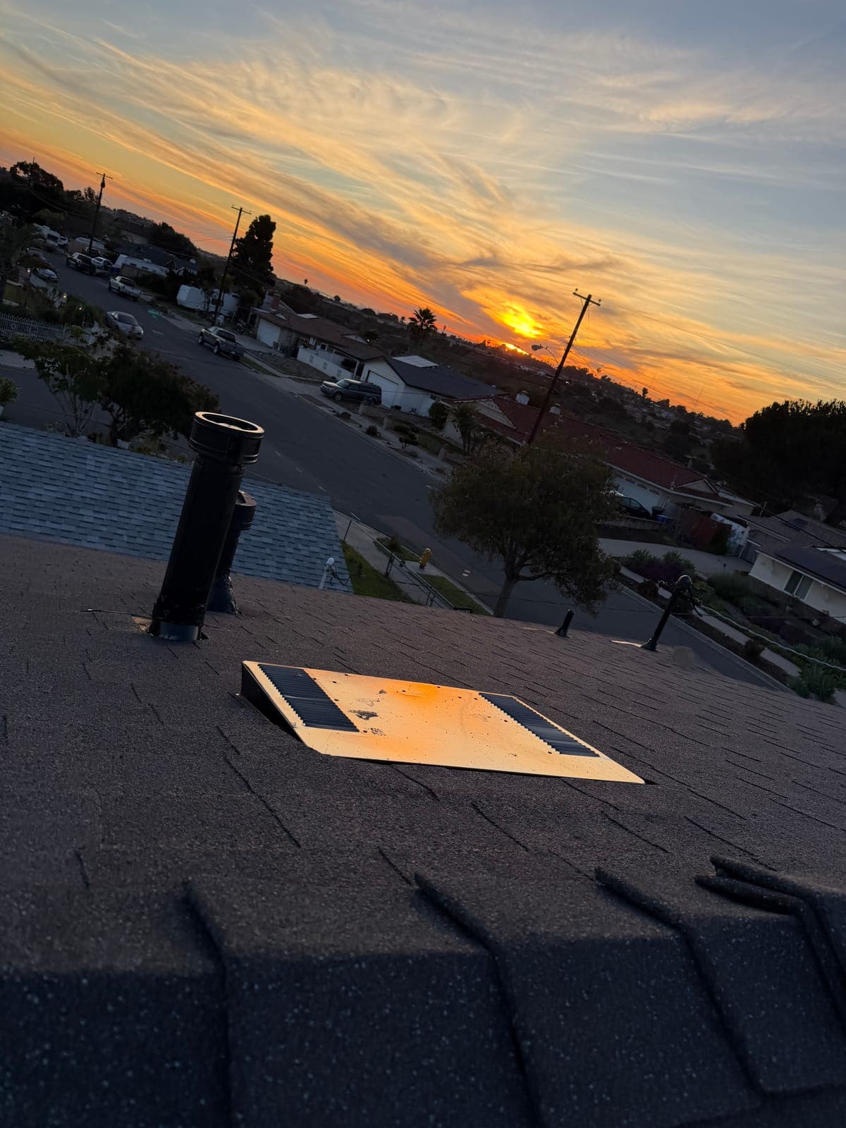 Roof vents and an attic fan on new shingles against a San Diego sunset